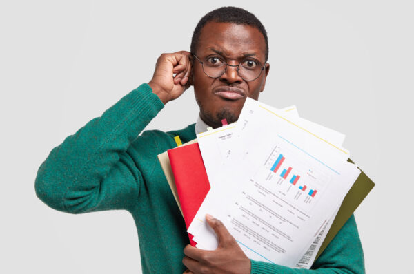Dissatisfied black man prepares accounting report, holds papers with inforgraphic, wears spectacles for good vision, scratches head in bewilderment, isolated over white background. Income analysis Dissatisfied black man prepares accounting report, holds papers with inforgraphic, wears spectacles for good vision, scratches head in bewilderment, isolated over white background. Income analysis